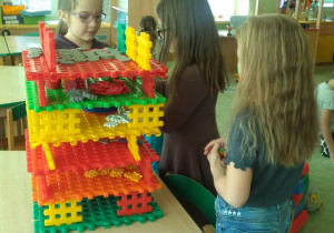 Dziewczynki bawią się przy stoliku zbudowaną z klocków budowlą.